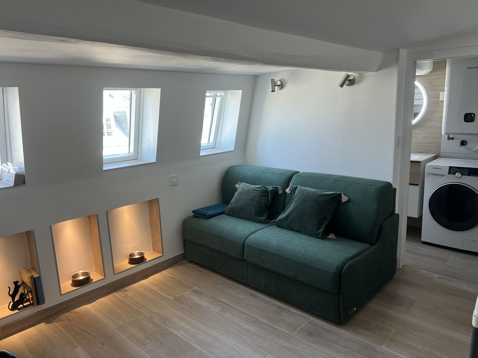 Après rénovation : pièce lumineuse sous les toits, canapé vert et rangements sur mesure